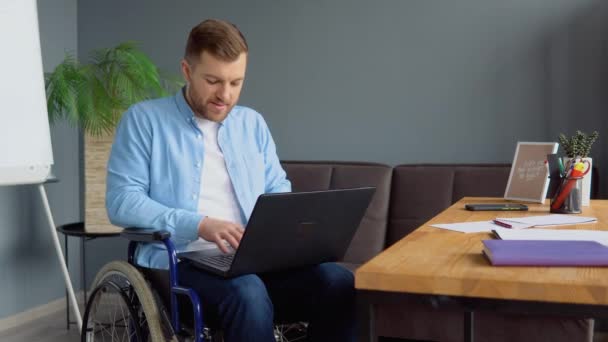 Студент-мужчина учится онлайн с помощью ноутбука, печатая сидя в инвалидной коляске в квартире, занятой дистанционным образованием. Концепция технологии и инвалидности — стоковое видео
