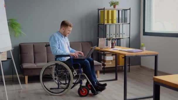 Osoba se zdravotním postižením na volné noze pracuje s notebookem psaní sedí na invalidním vozíku v kanceláři. Koncept práce na dálku a zdravotního postižení — Stock video