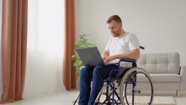 Фрілансер з обмеженими можливостями працює з ноутбуком, який сидить у інвалідному візку вдома. Дистанційна робота та концепція інвалідності — стокове відео