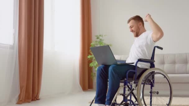 Vrolijke gelukkige gehandicapte verheugt zich op goed nieuws tijdens het zitten in een rolstoel met laptop — Stockvideo