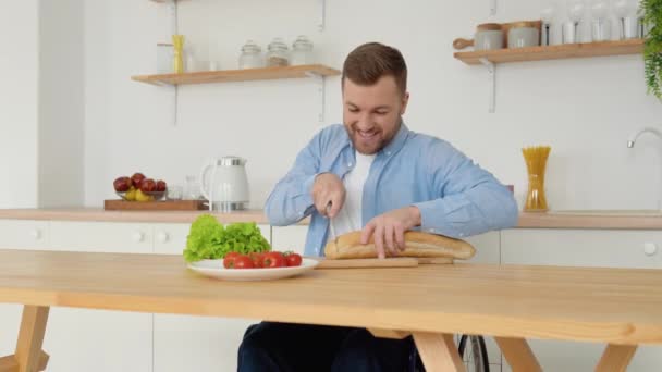 Χαρούμενο άτομο με ειδικές ανάγκες σε αναπηρικό καροτσάκι κόβει ψωμί στην κουζίνα — Αρχείο Βίντεο