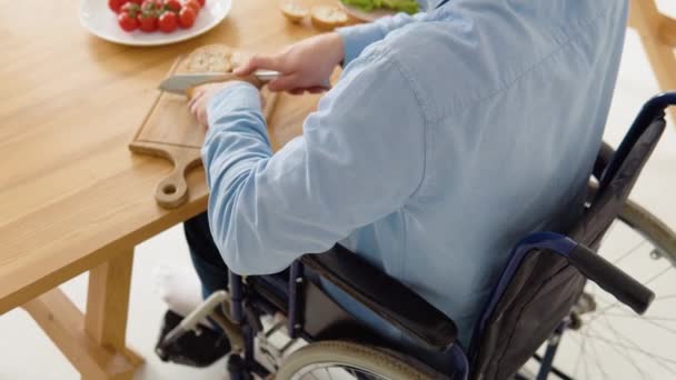 Primer plano de una persona discapacitada en silla de ruedas cortando pan en la cocina. Concepto de inclusión y discapacidad — Vídeo de stock