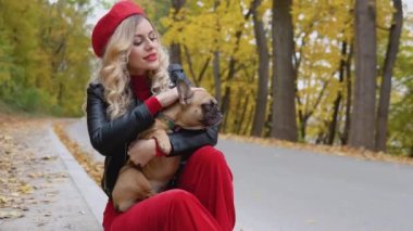 Kırmızı elbiseli güzel sarışın kadın kollarında bir buldog tutuyor.