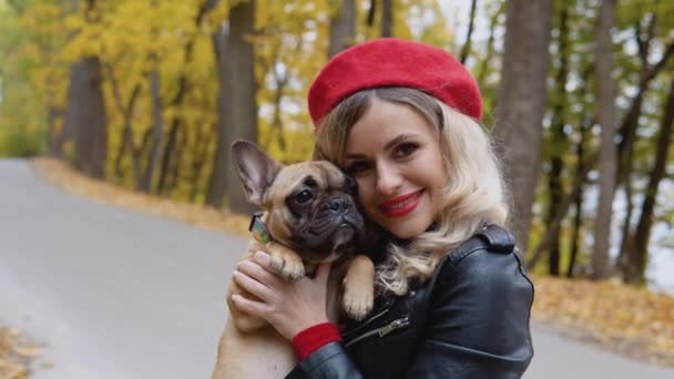 Portret van een lachende vrolijke vrouw met grappige franse bulldog in het najaarspark — Stockvideo