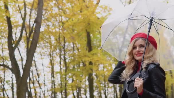 Sorrindo mulher alegre feliz em um terno vermelho e uma jaqueta de motociclista com um guarda-chuva transparente em um dia chuvoso. Doenças sazonais, tosse, frio — Vídeo de Stock