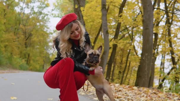 Jeune belle femme marchant dans un parc d'automne avec un drôle de bulldog français — Video