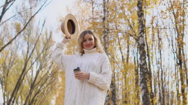 Beyaz kazaklı güzel sarışın kadın sonbahar parkında kahverengi şapka takıyor. — Stok video