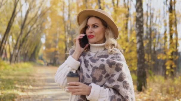 Красивая блондинка в коричневой шляпе говорит по телефону в осеннем парке — стоковое видео