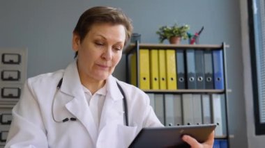 Kıdemli bayan doktor çevrimiçi video görüşmesi yapıyor. Kafkasyalı kadın terapist uzaktan sohbette kamerayla konuşuyor.