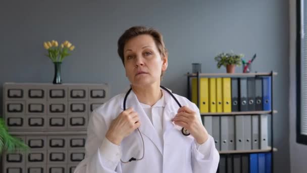 Positieve huisarts close-up gezicht portret. gelukkig senior europees vrouw arts dragen wit medisch jas en stethoscoop kijken naar camera — Stockvideo