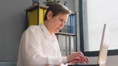 Kıdemli kadın dizüstü bilgisayarın arkasında çalışıyor. Uzak çalışma kavramı