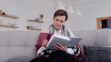 Evde kanepede otururken kıdemli bir kadın kitap okuyor. Kendini karantinaya almış bir kadının emeklilik hayatı