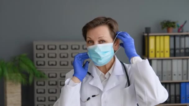La doctora senior se pone una máscara azul protectora. Protección contra virus — Vídeos de Stock