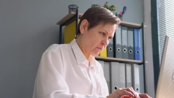 Una mujer mayor trabaja detrás de un portátil. Concepto de trabajo remoto — Vídeos de Stock