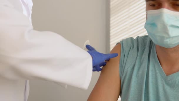 Starsza pielęgniarka podająca szczepionkę antywirusową Covid-19 lub szczepionkę przeciw grypie młodemu pacjentowi nosi maskę ochronną przed chorobami wirusowymi w klinice lub gabinecie szpitalnym. Koncepcja szczepień — Wideo stockowe