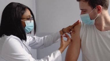 Genç Hintli hemşire genç erkek hastaya Covid-19 ya da grip aşısı yaparken sağlık kliniğinde ya da hastane ofisinde yüz maskesi takıyor. Aşılama kavramı