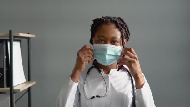 Positiv afrikansk kvinnlig läkare tar bort en medicinsk mask på kliniken. Slut på karantänen. Stoppa viruset — Stockvideo