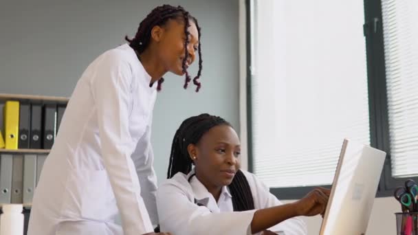 Two african women students discussing patient treatment plan showing something on laptop. Online treatment — Stock Video