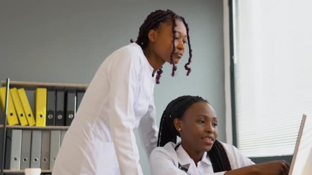 Zwei afrikanische Studentinnen diskutieren einen Behandlungsplan für Patienten und zeigen etwas auf einem Laptop. Online-Behandlung — Stockvideo