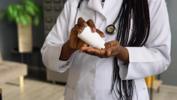Beyaz önlüklü Afrikalı Amerikalı kadın doktor kavanozdan hap alıyor. Ellerin görüntüsünü kapat — Stok video