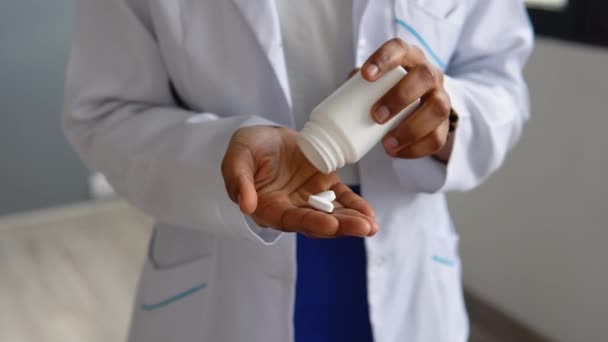 Η Αφροαμερικανή γιατρός με το άσπρο παλτό παίρνει χάπια από ένα βάζο. Κλείσιμο προβολής των χεριών — Αρχείο Βίντεο