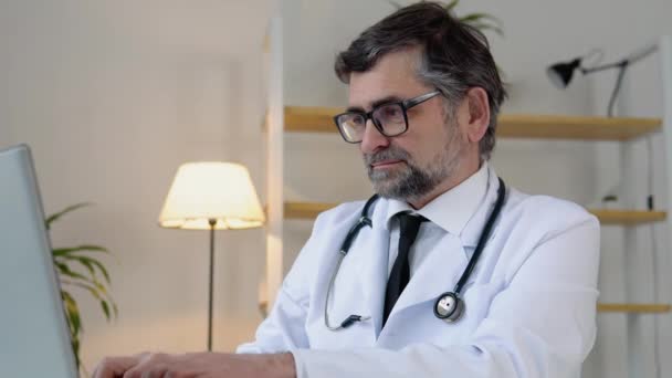 Starszy lekarz 50s pracuje w laptopie. Stary, dojrzały lekarz terapeuta pracujący w biurze — Wideo stockowe