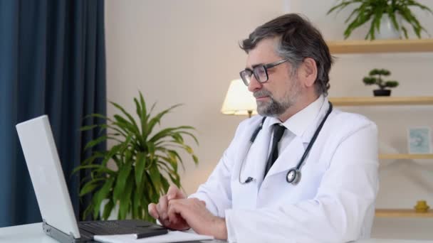 Médico principal hablando durante el chat de vídeo en el portátil — Vídeos de Stock