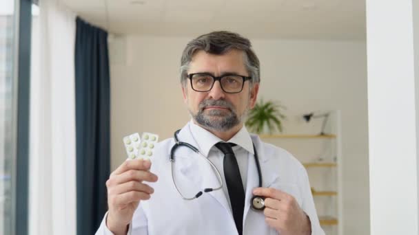 Starszy lekarz farmaceuta konsultant pokazuje dwie paczki tabletek i uśmiecha się przed kamerą. Koncepcja medycyny i opieki zdrowotnej, edukacji medycznej, sektora farmaceutycznego — Wideo stockowe