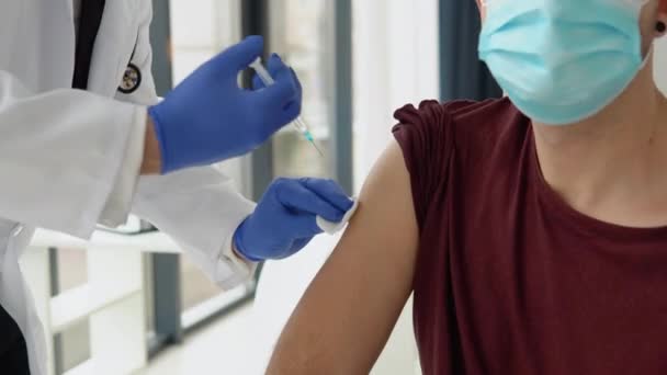 Lékař podávající přípravek Covid-19 nebo vakcínu proti viru chřipky mladému pacientovi mužského pohlaví nosí na klinice nebo v nemocničním úřadě ochranu před virovou chorobou. Koncepce očkování — Stock video