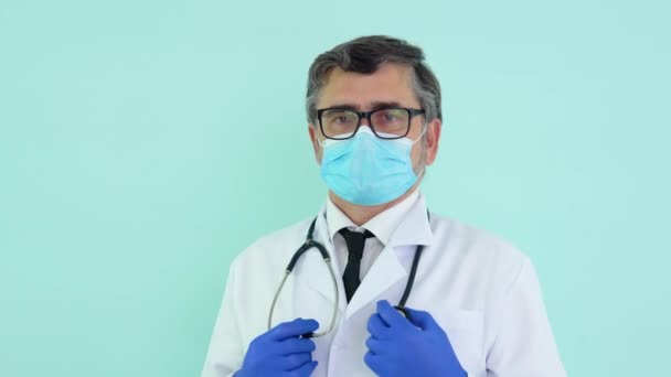 Portrait d'un médecin senior en costume blanc et masque de protection sur fond bleu — Video