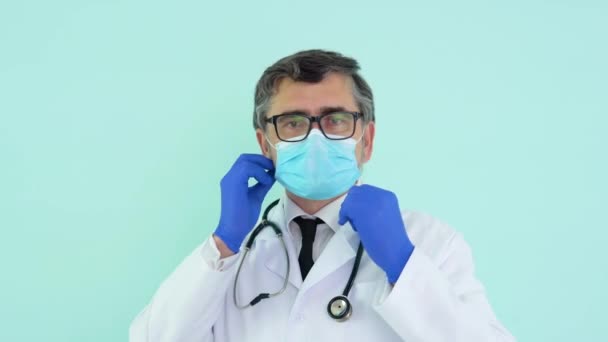 El médico senior se quita una máscara médica sobre fondo azul. Fin de la cuarentena. Detener virus — Vídeos de Stock