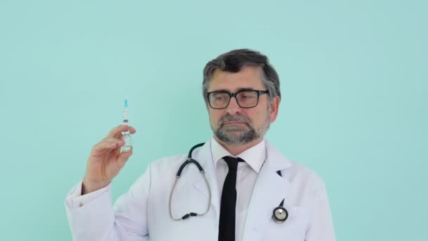 Läkaren håller en spruta och en vaccinflaska på sjukhuset på blå bakgrund. Hälsa och medicinska begrepp — Stockvideo