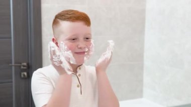 Banyodaki komik çocuk yüzünü tıraş köpüğüyle boyuyor, çocuk yetişkin bir babayı taklit ediyor.
