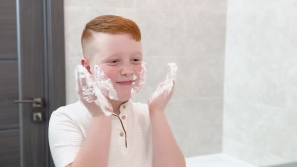 Забавный мальчик в ванной мажет лицо кремом для бритья, ребенок подражает взрослому папе, который бреется — стоковое видео