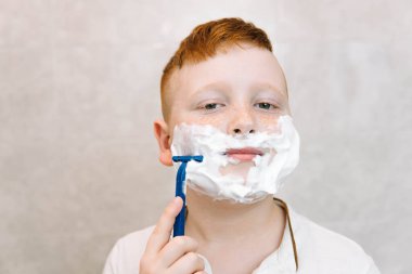 Küçük çocuk yüzünü banyoda tıraş ediyor. Komik çocuk banyoda tıraş olurken eğleniyor.