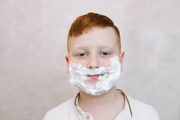 Забавный мальчик в ванной с кремом для бритья на лице — стоковое фото