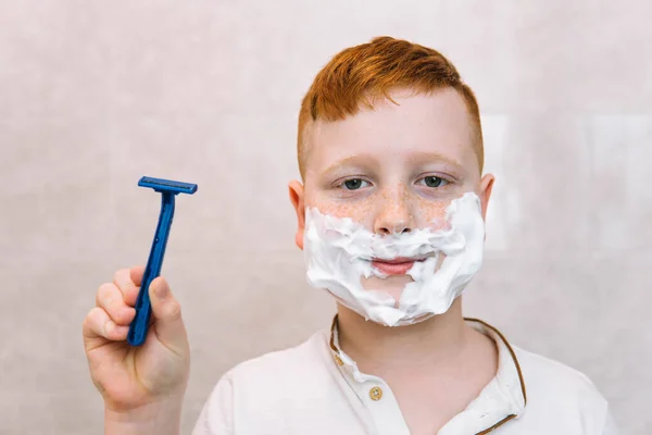 Morsom gutt i badekaret med barberskum i ansiktet og barberblad – stockfoto