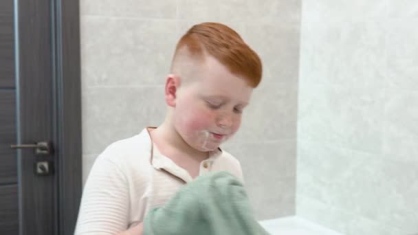 Kleiner Junge wischt sich nach der Rasur das Gesicht mit einem Handtuch ab — Stockvideo