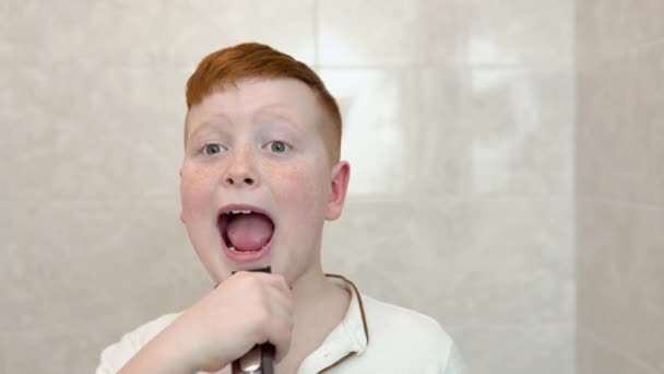 Lille dreng barberer sit ansigt med elektrisk barbermaskine på badeværelset. Sjov dreng har det sjovt, mens han barberer sig i badeværelset – Stock-video