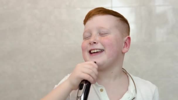 Мальчик бреет лицо электрической бритвой в ванной. Смешной мальчик веселится, когда бреется в ванной — стоковое видео