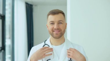 Beyaz önlüklü başarılı bir doktor kameraya bakar ve hastane ofisinde gülümser.
