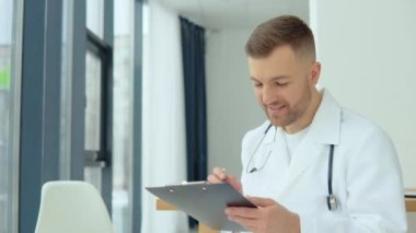 Erkek doktor, muayenehanesinde hastanın tıbbi geçmişini yazıyor.