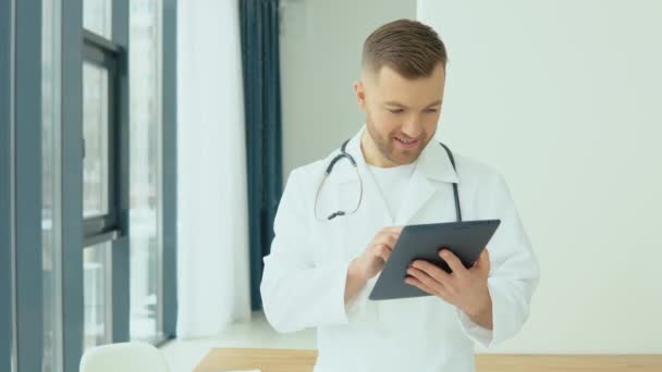 Młody lekarz bada historię choroby w tabletce przed przybyciem pacjenta — Wideo stockowe
