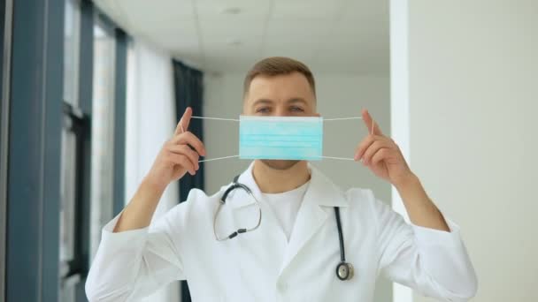 A férfi orvos felvesz egy kék maszkot a klinikán. Vírusvédelem — Stock videók