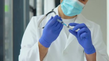 Koruyucu maskeli genç bir doktor şırıngaya aşı çekiyor.