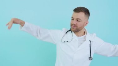 Steteskoplu, beyaz ceketli, mavi arka planda dans eden neşeli başarılı doktor.