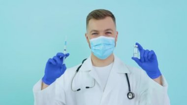 Doktor elinde aşı ve şırıngayla mavi arka planda bir ampul tutuyor.