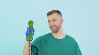 Yeşil üniformalı ve mavi eldivenli dost canlısı bir doktor eski bir telefonu elinde tutuyor ve onu işaret ediyor.