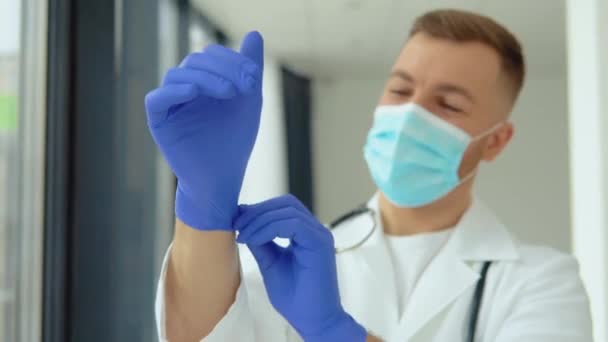 Νεαρός γιατρός με προστατευτική μάσκα φοράει ιατρικά γάντια — Αρχείο Βίντεο