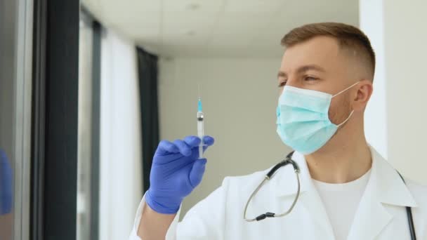 Jovem médico com uma máscara protetora com uma seringa de vacina nas mãos — Vídeo de Stock